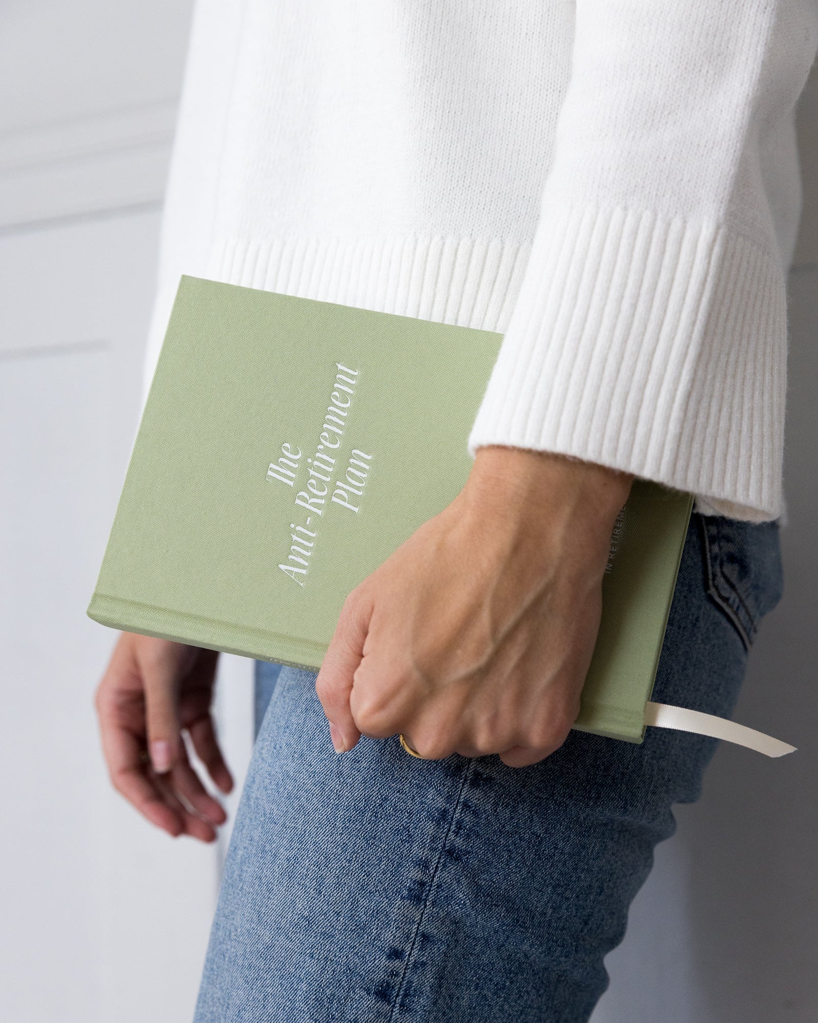 Person holding a green book titled 'The Anti-Retirement Plan' against a white background