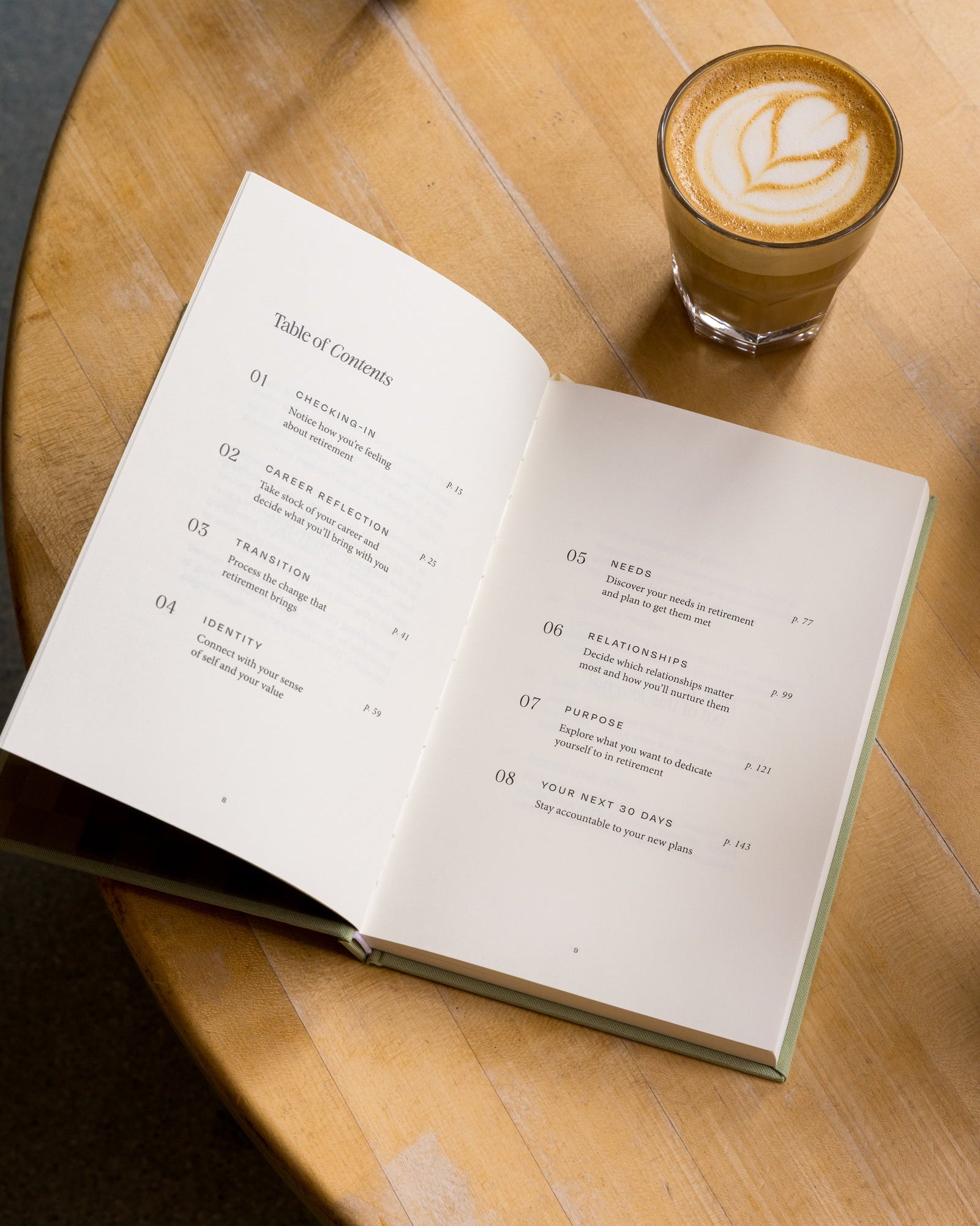 Open Anti-Retirement Plan on a wooden table with a glass of cappuccino.