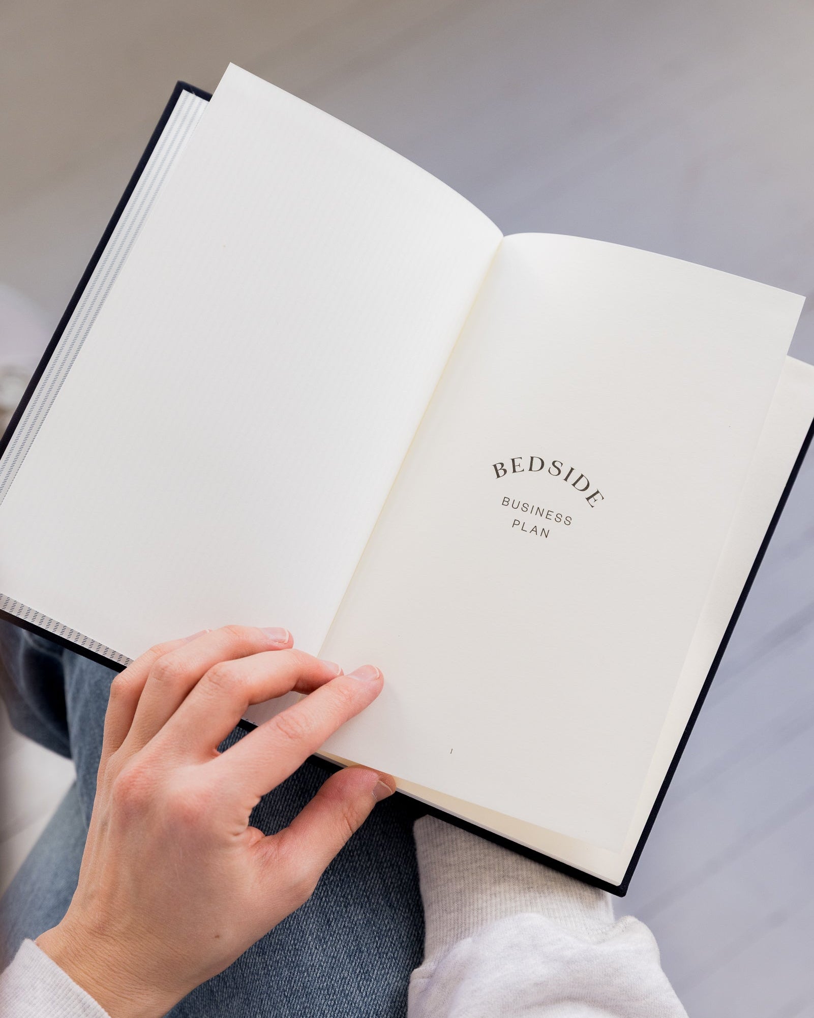 Person holding an open Bedside Business Plan on a light surface.