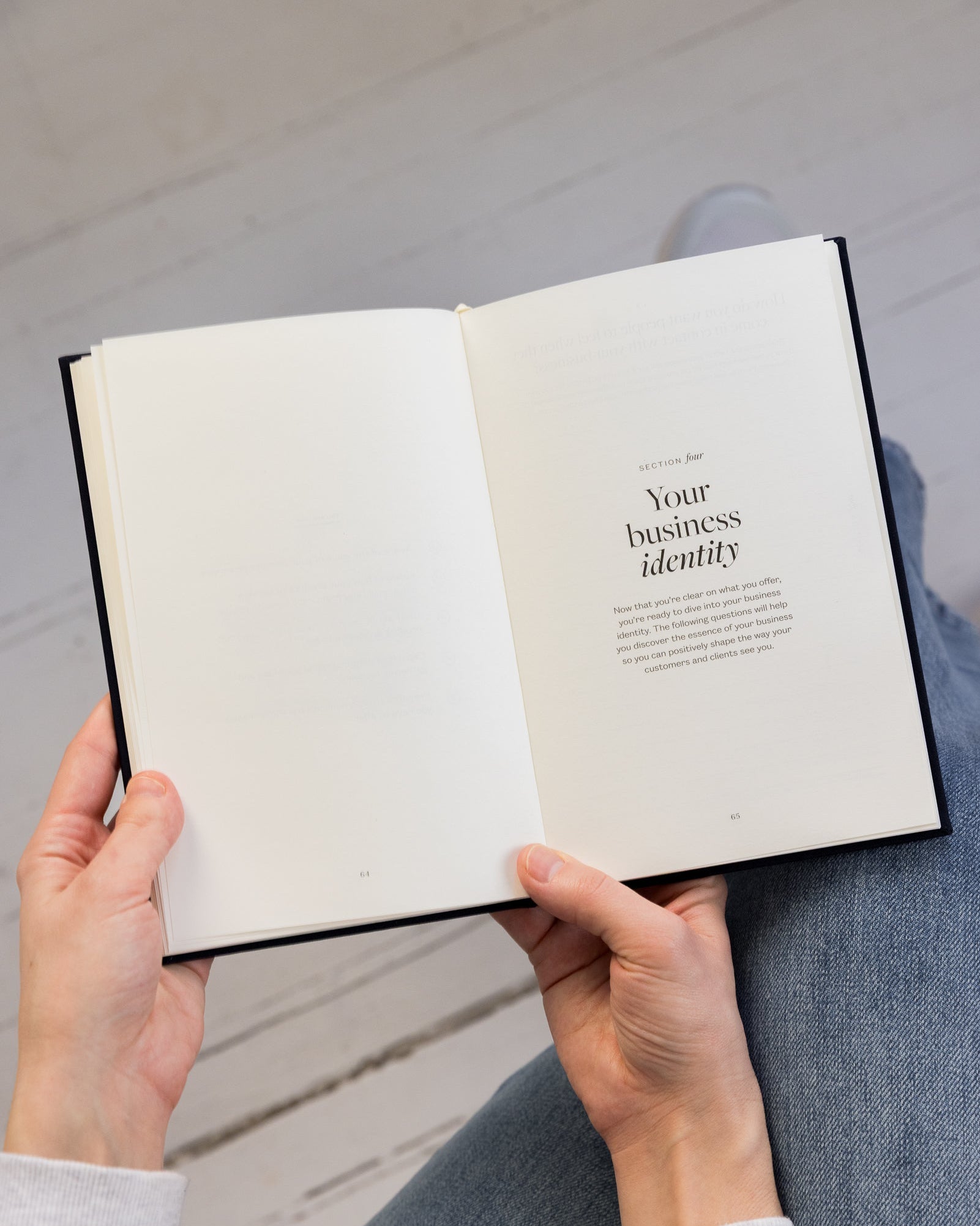 Person holding an open Bedside Business Plan guided journal with text on a wooden floor.