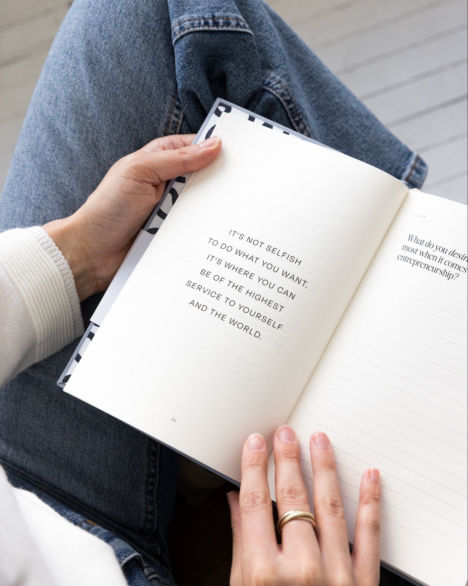Person holding Employee to Entrepreneur guided journal with text, sitting on a wooden floor.