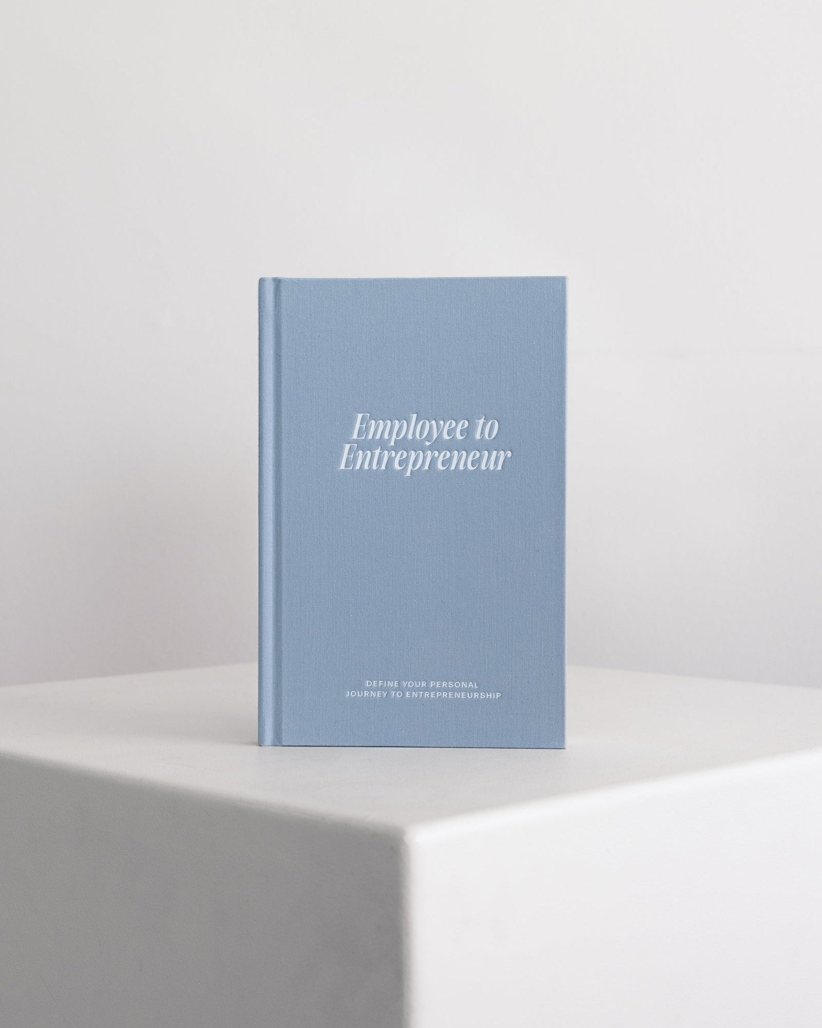 Blue guided journal titled 'Employee to Entrepreneur' on a white surface with a light gray background