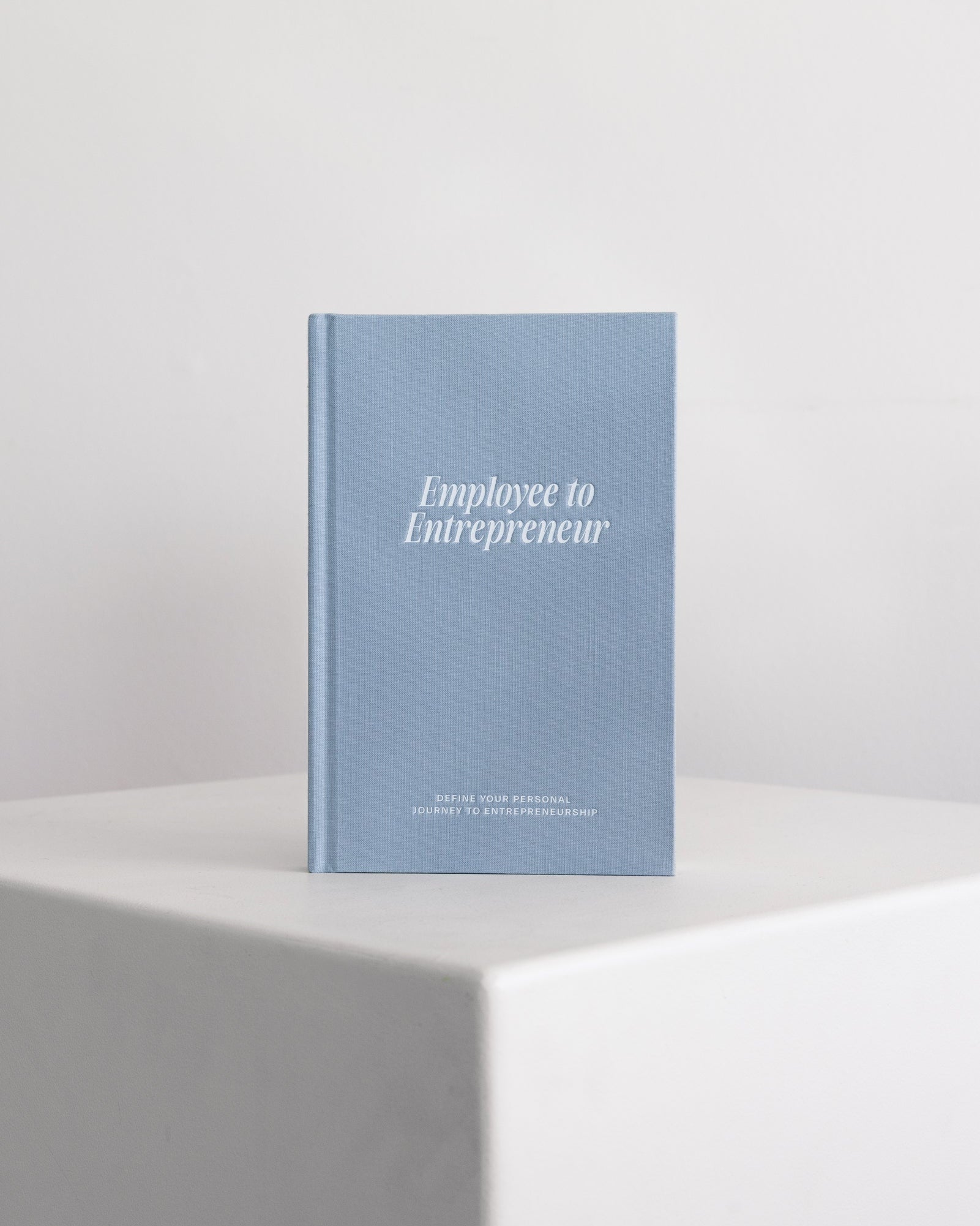 Blue guided journal titled 'Employee to Entrepreneur' on a white surface with a light gray background